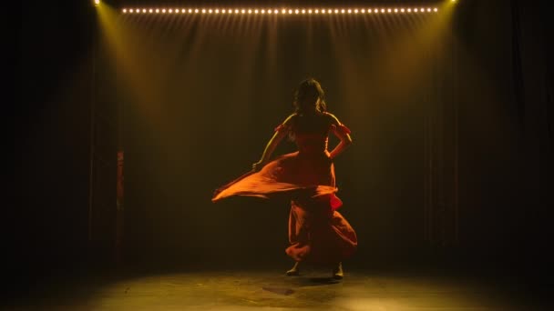 Karanlık bir stüdyoda ateşli bir şekilde flamenko yapan orta yaşlı bir kadının silueti. Yanan esmer, uzun kırmızı elbiseli, dumanlı arka planda, sarı ışıklı. Yavaş çekim. — Stok video