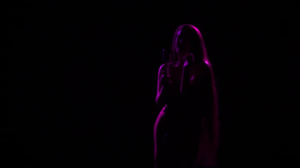 An attractive woman with long hair is silhouetted in a sexy motion near a vintage microphone. The soloist sings in the dark with studio light. Close up. — Stock Video