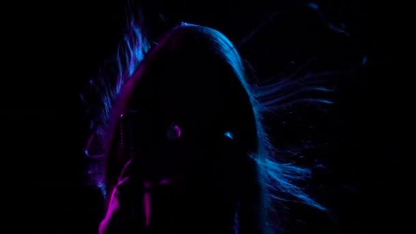 A lovely brunette holds a vintage microphone in her hands and sings. A womans hair flutters in the wind. Silhouette in a dark studio with backlight. Close up. — Stock Video