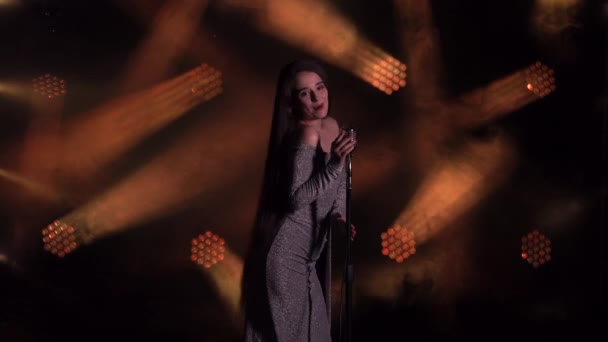 Professional music. Portrait of emotional sexy singer singing a song into a vintage microphone. Dark studio with smoke and bright lights. Side view of a woman in a shiny dress close up. — Stock Video