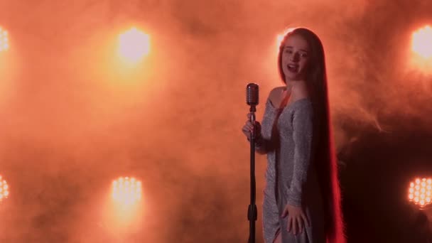 Sexy cantante femminile glamour si esibisce sul palco in un abito da sera lungo. Una donna canta una canzone in un microfono vintage su uno sfondo di fumo e luce da studio. Da vicino.. — Video Stock