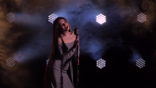 Um belo jovem vocalista com cabelos longos dá um concerto no palco no escuro sob a luz de muitos holofotes. Um cantor em um vestido da tarde canta no palco na fumaça. Fechar. — Vídeo de Stock