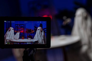 Sahne arkasında, beyaz bir çarşaf ve kulaklık takmış hayalet gibi giyinmiş biri mikrofonun önünde oturup Cadılar Bayramı teması üzerine komik bir podcast hazırlıyor..