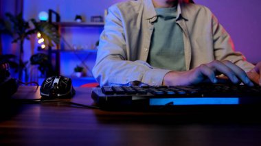 Renkli ışıklandırma ve modern çevresel özelliklere sahip bir oyun ayarında bilgisayar klavyesinde yazan bir kişi.