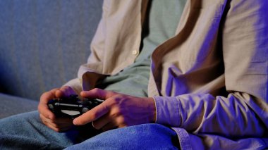 Bir insan rahatça otururken oyun kontrolörüyle oyun oynayarak boş zamanlarının tadını çıkartıyor..