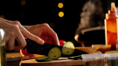 Bir şef ustalıkla taze bir salatalığı keskin bir bıçakla loş bir mutfakta, tahta bir tahtanın üzerinde doğruyor..