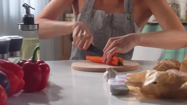 Parlak bir mutfakta havucu dilimleyen bir kadın taze malzemelerle birlikte pişirmeye hazır..