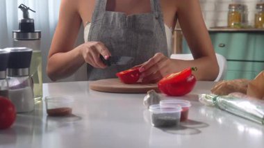 Önlüklü bir kadın modern bir mutfak ortamında kırmızı biber dilimliyor..
