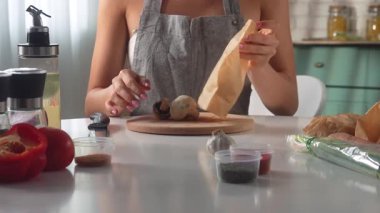 Önlüklü bir kadın modern bir mutfak ortamında Şampiyon mantarlarını kesiyor..