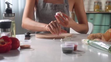 Bir kadın sıcak bir mutfakta otururken baharatlı bir yemek hazırlamak için sarımsak soyar. Dişi, yemek yapmak için malzemeleri hazırlar..
