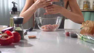 Bir kadın dilimlenmiş tavuğa tuz, biber ve çeşitli baharatlar serpiyor. Kadın sıcak, aydınlık bir mutfakta otururken sağlıklı bir öğle yemeği hazırlıyor..