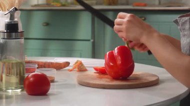 Önlüklü bir kadın modern bir mutfak ortamında kırmızı biber dilimliyor..