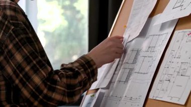 Bir kişi tasarım ve planlamayı vurgulayarak, bir mantar panoya tutturulmuş ayrıntılı mimari planları gözden geçirir. Tasarım, mimari süreç veya eğitim kavramı.