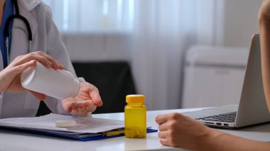 Beyaz önlüklü bir doktor ilaç şişesini muayene ediyor. Masasında tıbbi aletler ve evraklar var..