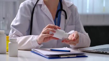 Beyaz önlüklü bir doktor bir ilaç şişesini inceler, anket formuna notlar alır ve verileri bir dizüstü bilgisayara kaydeder. Tıbbi aletler ve belgeler masanın üzerinde..