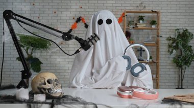 Hayalet gibi giyinmiş, beyaz çarşaf giymiş biri mikrofonun önünde oturup Cadılar Bayramı teması üzerine komik bir podcast ya da blog hazırlıyor. Komedi, medya ve korkunç temalar için ideal.