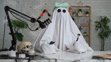 Beyaz bir sayfadaki hayalet güzellik hakkında konuşuyor ve Gua Sha kazıyıcı tutarken yüz bakımından bahsediyor. Süslü bir kayıt stüdyosunda neşeli bir Cadılar Bayramı konsepti.