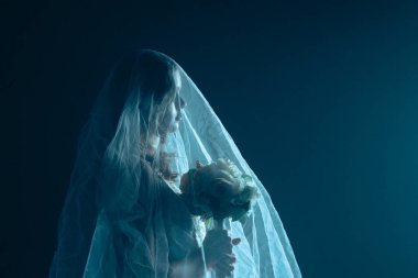 Karanlık bir sahnede tüyler ürpertici mavi bir ışık tarafından aydınlatılan şeffaf bir duvakla kaplanmış ölü bir gelin figürünün yer aldığı ürkütücü bir Cadılar Bayramı sahnesi. Hayalet gelin elinde bir buket tutuyor..