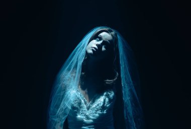 Karanlık bir sahnede tüyler ürpertici bir Cadılar Bayramı sahnesi, şeffaf bir duvakla kaplanmış ölü bir gelin figürü, ürkütücü bir mavi ışıkla aydınlatılmış. Hayalet gelin korku, gizem ve doğaüstü bir atmosferi temsil ediyor..