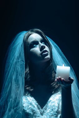 Karanlık bir sahnede tüyler ürpertici mavi bir ışık tarafından aydınlatılan şeffaf bir duvakla kaplanmış ölü bir gelin figürünün yer aldığı ürkütücü bir Cadılar Bayramı sahnesi. Hayalet gelin elinde yanan bir mum tutuyor..