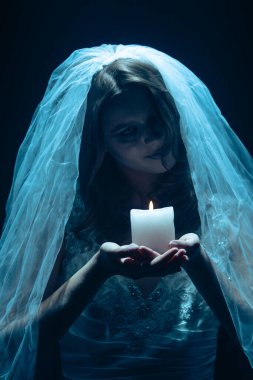 Karanlık bir sahnede tüyler ürpertici mavi bir ışık tarafından aydınlatılan şeffaf bir duvakla kaplanmış ölü bir gelin figürünün yer aldığı ürkütücü bir Cadılar Bayramı sahnesi. Hayalet gelin elinde yanan bir mum tutuyor..