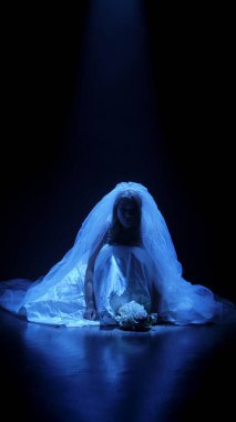 Karanlık bir sahnede tüyler ürpertici bir Cadılar Bayramı sahnesi, şeffaf bir duvakla kaplanmış ölü bir gelin figürü, ürkütücü bir mavi ışıkla aydınlatılmış. Hayalet gelin korku, gizem ve doğaüstü bir atmosferi temsil ediyor..