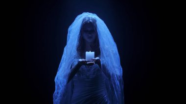 Karanlık bir sahnede tüyler ürpertici mavi bir ışık tarafından aydınlatılan şeffaf bir duvakla kaplanmış ölü bir gelin figürünün yer aldığı ürkütücü bir Cadılar Bayramı sahnesi. Hayalet gelin elinde yanan bir mum tutuyor..