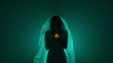 Karanlık bir sahnede tüyler ürpertici yeşil bir ışık tarafından aydınlatılan şeffaf bir duvakla kaplanmış ölü bir gelin figürünün yer aldığı ürkütücü bir Cadılar Bayramı sahnesi. Hayalet gelin elinde yanan bir mum tutuyor..