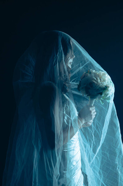 A spooky Halloween scene featuring a dead bride figure covered in a transparent veil, illuminated by an eerie blue light on a dark stage. The ghostly bride holds a bouquet in her hands.