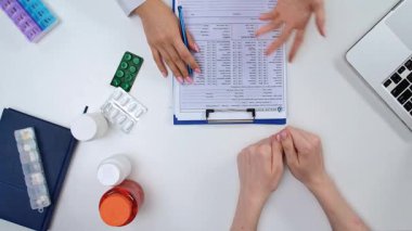 Tıp bürosundaki doktor masasının üst görüntüsü. Masanın üzerinde teşhis için tıbbi kayıtlar ve tedavi için ilaçlar var..