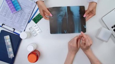 Bir doktor ve hasta, tıbbi tablolarla ve ilaçlarla çevrili bir göğüs röntgeni hakkında konuşuyorlar. Hastane ya da laboratuardaki tıbbi profesyoneller masasının en üst görüntüsü.