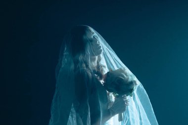 Karanlık bir sahnede tüyler ürpertici mavi bir ışık tarafından aydınlatılan şeffaf bir duvakla kaplanmış ölü bir gelin figürünün yer aldığı ürkütücü bir Cadılar Bayramı sahnesi. Hayalet gelin elinde bir buket tutuyor..