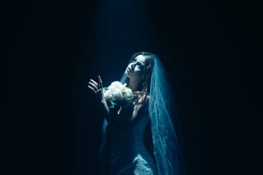 Karanlık bir sahnede tüyler ürpertici mavi bir ışık tarafından aydınlatılan şeffaf bir duvakla kaplanmış ölü bir gelin figürünün yer aldığı ürkütücü bir Cadılar Bayramı sahnesi. Hayalet gelin elinde bir buket tutuyor..