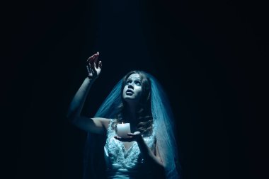 Karanlık bir sahnede tüyler ürpertici mavi bir ışık tarafından aydınlatılan şeffaf bir duvakla kaplı ölü bir gelin figürünün olduğu ürkütücü bir Cadılar Bayramı sahnesi. Hayalet gelin ışık huzmesine uzanıyor..