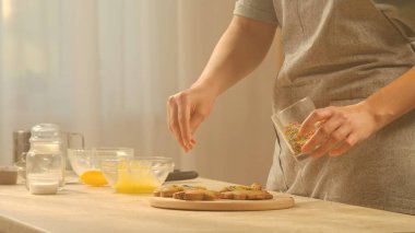 Bir insan taze pişmiş kurabiyeleri renkli şekerlerle süslüyor ve yaratıcı bir aşçılık süreci sergiliyor. Konforlu, parlak bir mutfakta ev yapımı pişmiş yiyecekler hazırlıyorum..