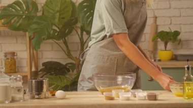 Bir kadın cam kasede spatulayla malzemeleri karıştırıyor ve hamurun içine yumurta atıyor. Çeşitli malzemelerle çevrili bir pasta şefi, yemek pişirme sanatından zevk alıyor. Evde pişirme ve pişirme süreci.