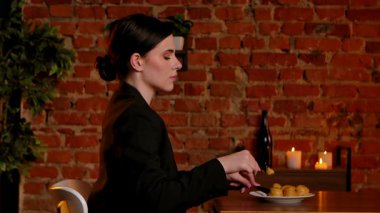 Bir kadın tatlı olarak kremalı pasta yer. Zarif bir kadın, tuğla duvarlar, mumlar ve yumuşak ışıklandırma olan samimi bir restoranda romantik bir akşam yemeğinden zevk alır. Yan görünüm.