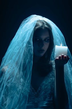 Karanlık bir sahnede tüyler ürpertici mavi bir ışık tarafından aydınlatılan şeffaf bir duvakla kaplanmış ölü bir gelin figürünün yer aldığı ürkütücü bir Cadılar Bayramı sahnesi. Hayalet gelin elinde yanan bir mum tutuyor..