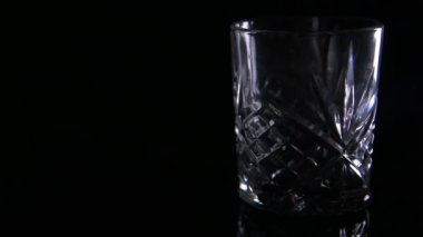 Işık, karanlık bir arka planda boş viski bardağının üzerinden geçiyor.