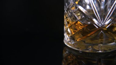 Karanlık yansıtıcı arka planda viskiyle dolu geleneksel cam bardağa yaklaş