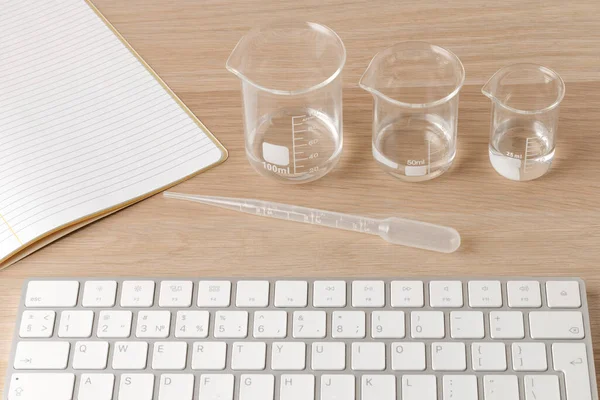 three measuring beakers with a measuring pipette with notebook and a keyboard