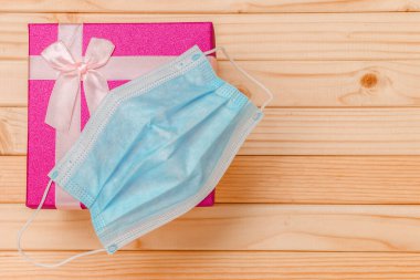 Tahta bir arka planda üzerinde yüz maskesi olan küçük dikdörtgen bir hediye kutusu.