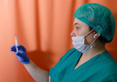 Koruyucu maske ve eldiven takan bir doktor salgın sırasında kovid 19 koronavirüs salgınına karşı aşı içeren bir şırınga gösteriyor.