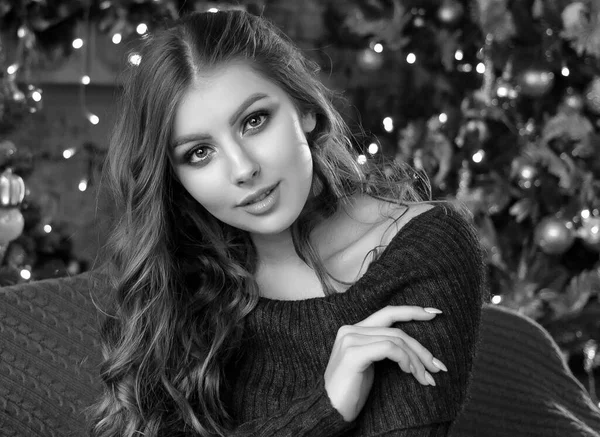 A young beautiful girl with loose hair close up sitting next to a Christmas tree with Christmas toys and garlands