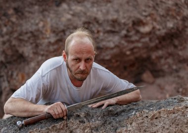 Savaştan sonra elinde bir hançerle dağlarda dinlenen savaşçı gezgin.