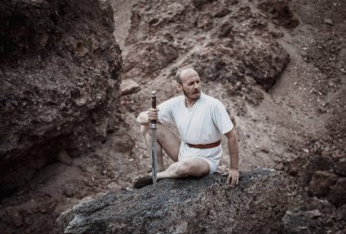 Savaştan sonra elinde bir hançerle dağlarda dinlenen savaşçı gezgin.