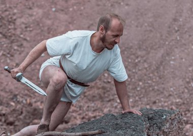 Savaştan sonra elinde bir hançerle dağlarda dinlenen savaşçı gezgin.