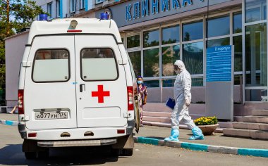 Bulaşıcı koruyucu tulumlu ve koruyucu maskeli bir doktor kovid 19 koronavirüs salgınının karantinası sırasında bir hastayı ziyaret etmek için ambulansa gider.