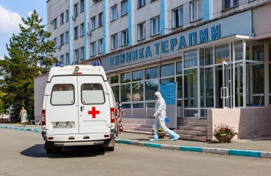 Bulaşıcı koruyucu tulumlu ve koruyucu maskeli bir doktor kovid 19 koronavirüs salgınının karantinası sırasında bir hastayı ziyaret etmek için ambulansa gider.