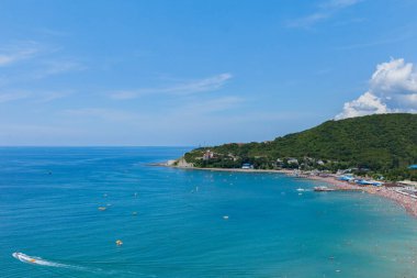 Dağın eteğinde turistlerle dolu bir plajı olan bir tatil beldesi.